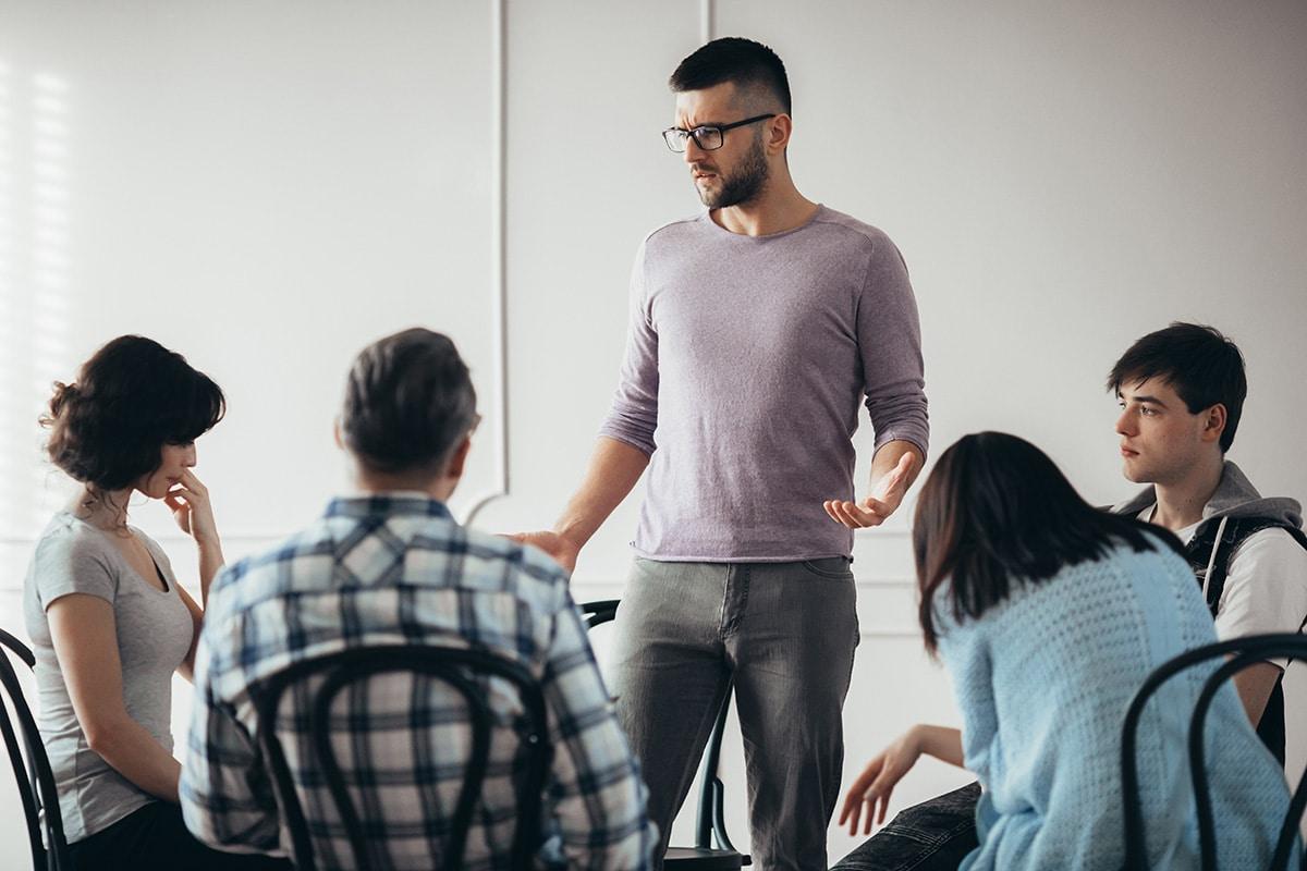 counselor talks to other patients in a group therapy circle about the effects of trauma