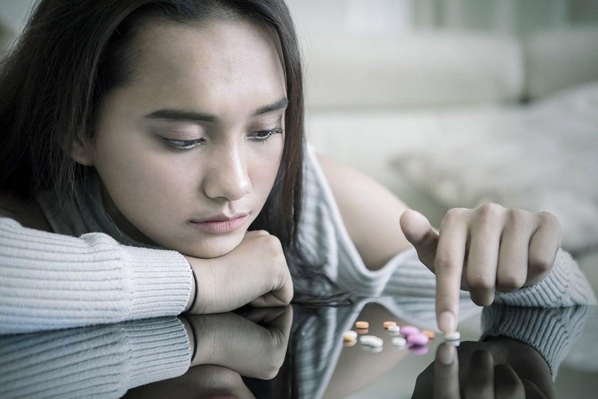 young girl picking out pills of designer drugs on coffee table